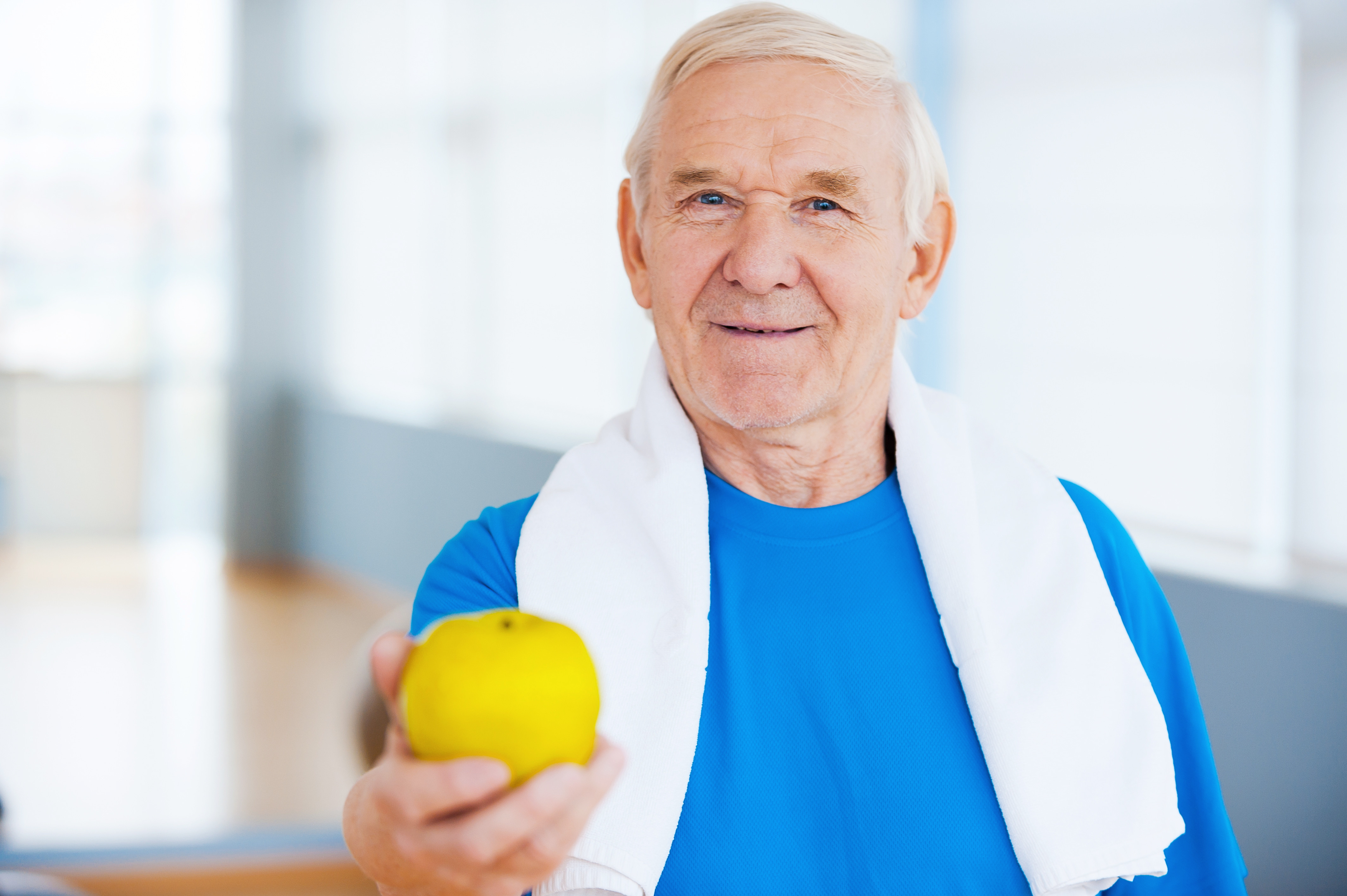 Senior mit blauem T-Shirt hält einen Apfel in die Kamera