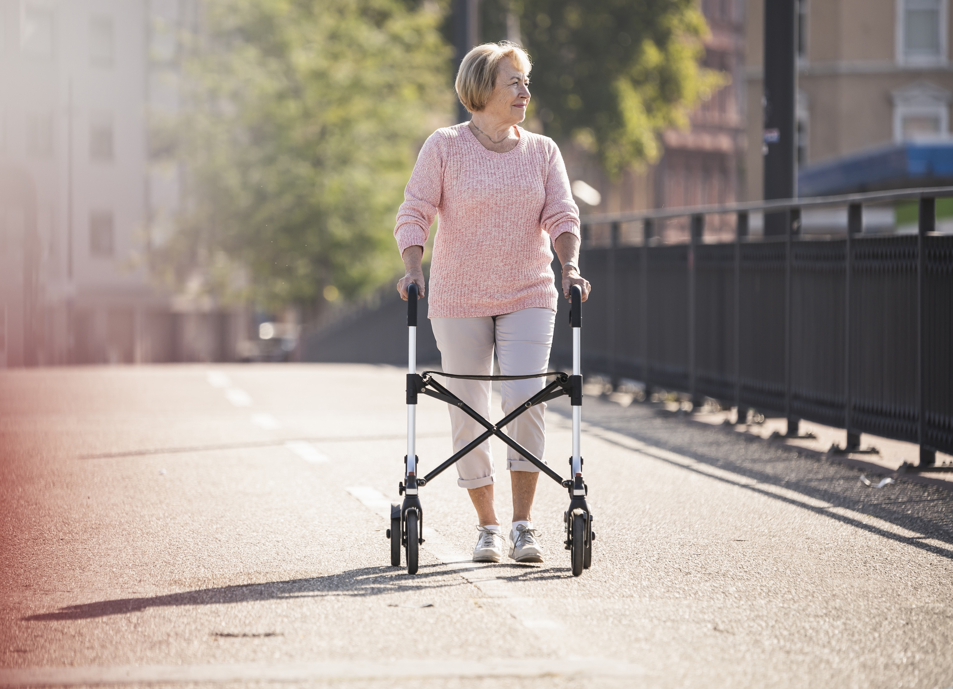 Frau spaziert an einem sonnigen Tag mit Rollator über eine Brücke
